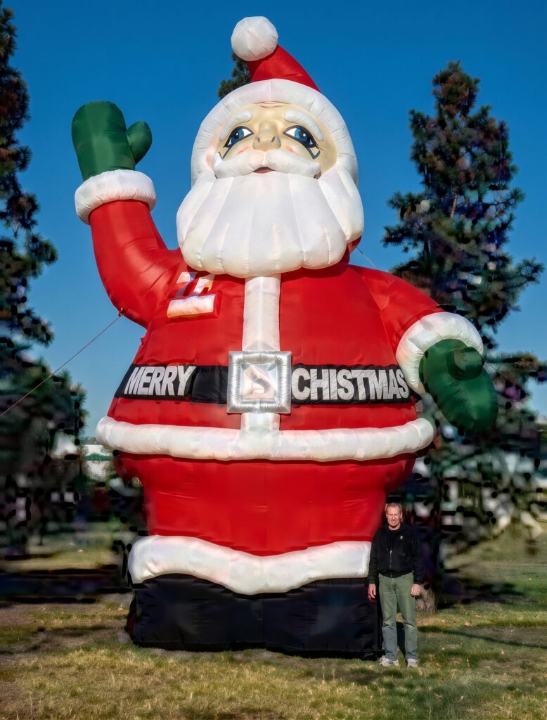 A giant inflatable Santa Claus waving, with a Merry Christmas belt
